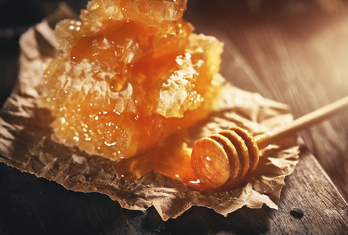 나무탁자위 종이 위에 벌집꿀과 꿀이 묻은 꿀스푼 사진