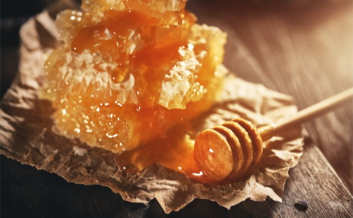 나무바닥에 종이를 깔고 벌꿀집과 꿀스틱에 꿀이 묻어있는 사진