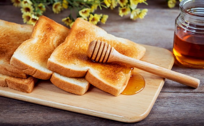 도마위에 구운식빵들이 있고 그 위에 꿀이 묻은 꿀 스틱이 있는 사진